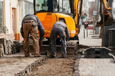 İşçiler, sarı bir traktöre taş yığıyor.