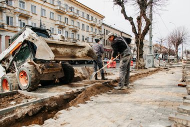 Küçük bir traktör işçilere kum getirdi; kentte yol onarımı devam ediyor