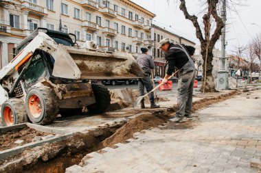 Küçük bir traktör işçilere kum getirdi; kentte yol onarımı devam ediyor