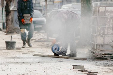 İşçi kaldırım taşlarını keser ve çok toz yapar.