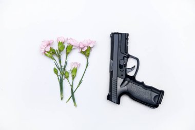 Siyah silah beyaz arka planda çiçeklerle yatar.