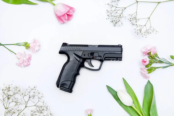 The gun lies on a background of flowers. Romantic composition of weapons