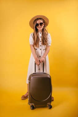 Sarı arka planda bavulu olan şapkalı genç ve genç bir kız.