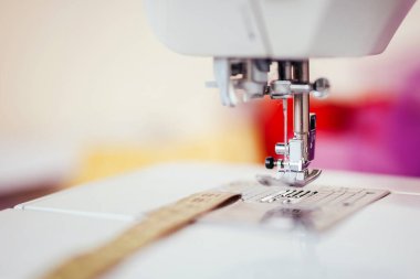 Dikiş makinesine iğne batırılmış, arka planda bulanık ayak.