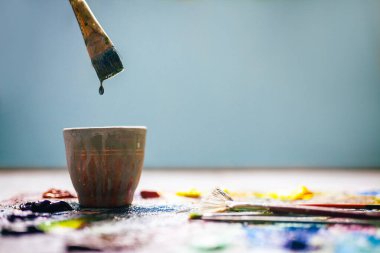 Ressam fırçası boyaya batırılmış, tabağın üzerinde bir damla asılı. Bulanık arkaplan