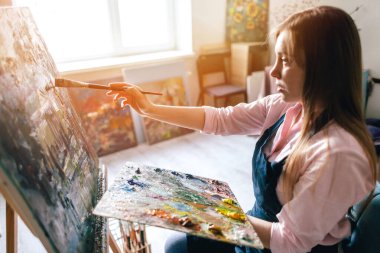 Ressam kız tuval üzerinde fırçayla manzara resmediyor.