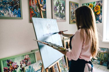 Kız ressam bir sehpanın yanında durur ve resim çizer.