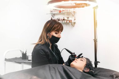 Profesyonel güzellik uzmanı ofisteki bir hastaya kaş dövmesi yapıyor.