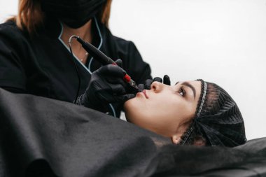 Kız makyajcı dudakları dövme makinesi yapıyor.