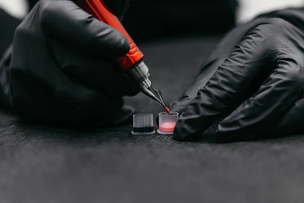 Makeup master beautician dips the tip of a tattoo machine into a pigment