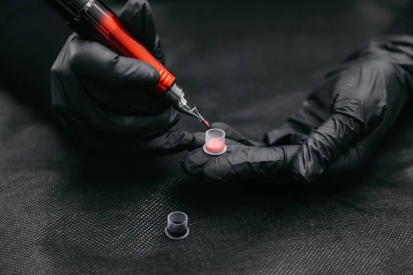 Master beautician makeup dips the tip of a tattoo machine in pink pigment