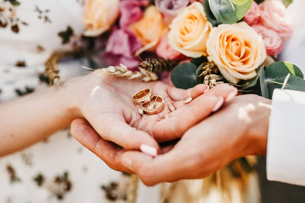 結婚式のカップルは 花の背景に金の指輪を手に持っています — ストック写真
