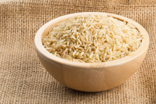 Natural brown uncooked rice in wooden bowl on burlap — Stock Photo, Image