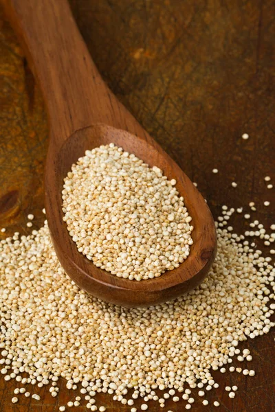 Raaka, kokonainen, jalostamaton kvinoan siemen puulusikassa villisikalla — kuvapankkivalokuva
