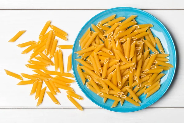 Montón de pasta de penne seca, cruda, sin cocer en el plato en la mesa — Foto de Stock