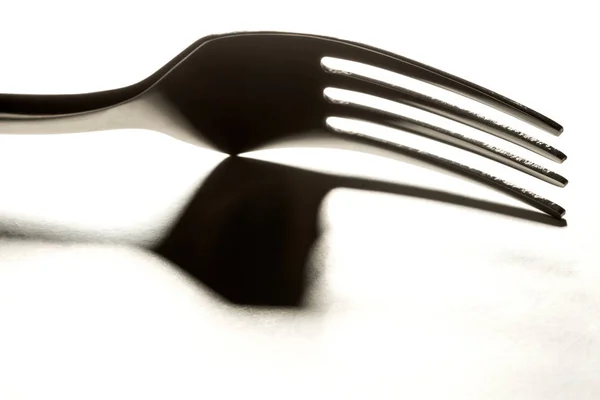 Cierre de tenedor metálico retroiluminado con sombra sobre blanco —  Fotos de Stock