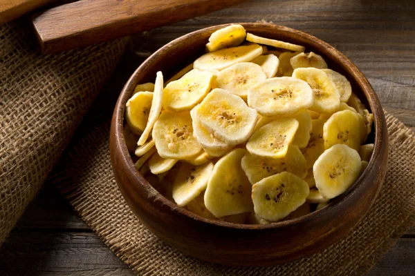 Montón de chips de plátano seco snack en un tazón de madera sobre una mesa oscura —  Fotos de Stock