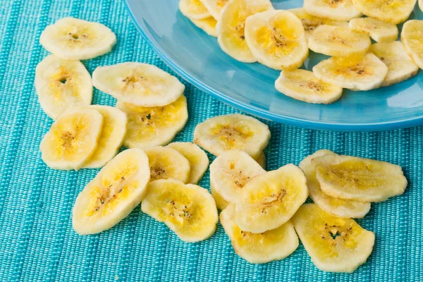Heap of dried banana chips snack on blue turquoise plate and mat — Stock Photo, Image
