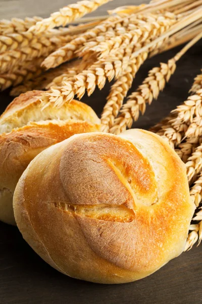 Bündel von ganzen, frisch gebackenen Weizenbrötchen mit Weizenähren auf dunklem — Stockfoto