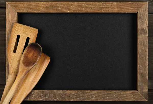 Wooden kitchen cooking tools on empty menu board with copy space — Stock Photo, Image