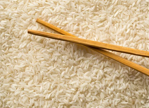 White uncooked, raw long grain rice full frame with chopsticks — Stock Photo, Image