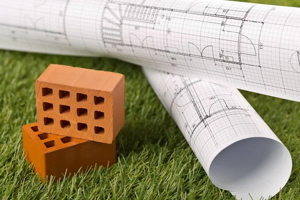 Architectural blueprints with miniature bricks on green grass — Stock Photo, Image