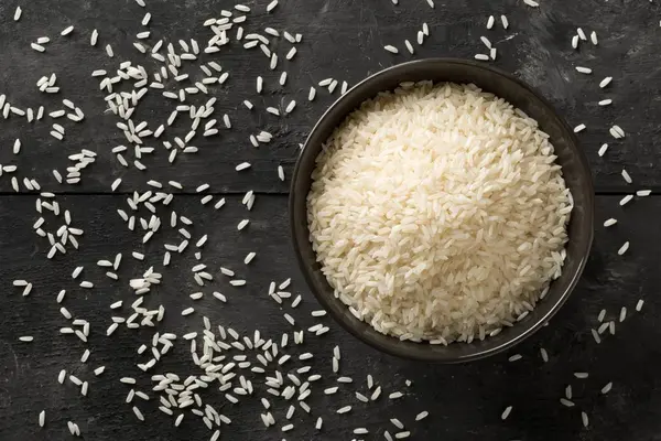 White uncooked, raw long grain rice in black bowl — Stock Photo, Image