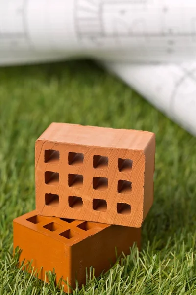 Építészeti tervrajzok miniatűr téglákkal zöld füves háttér — Stock Fotó
