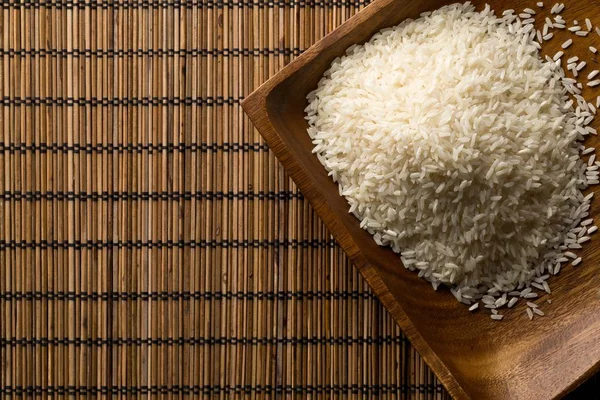 Arroz blanco sin cocer y crudo de grano largo en un tazón de madera sobre estera de bambú — Foto de Stock