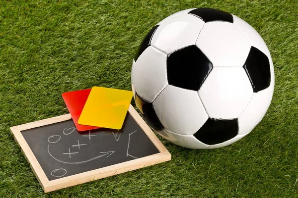 Pelota deportiva de fútbol con estrategia de juego dibujo pizarra y tarjetas árbitro amarillo y rojo en el fondo de hierba — Foto de Stock