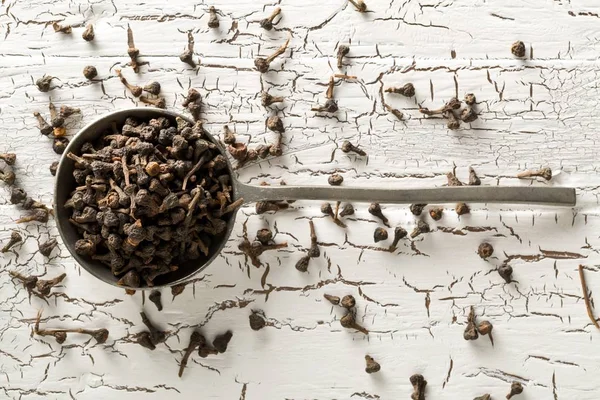 Heap of raw, dried cinnamon blossom buds spice in metal scoop on rustic white table background — Stock Photo, Image