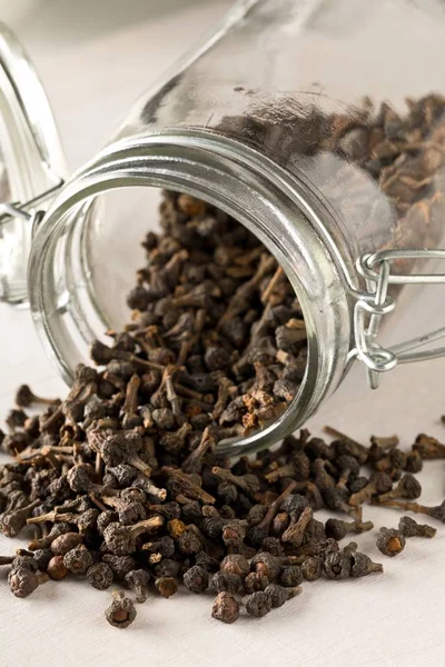 Heap of raw, dried cinnamon blossom buds spice in glass storage jar on white table background — Stock Photo, Image