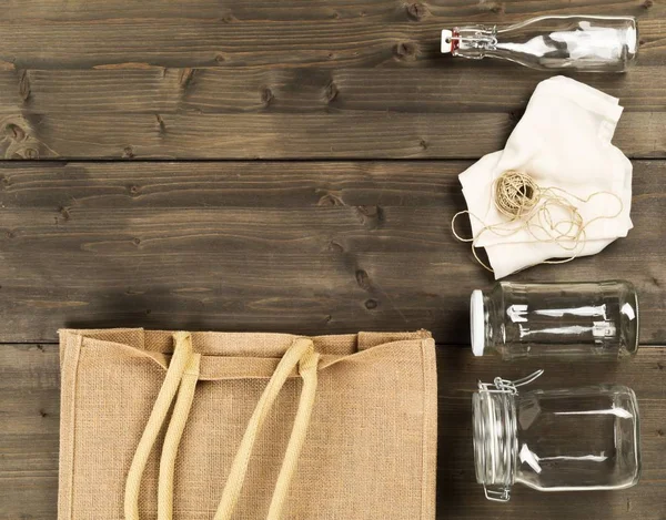 Zero waste or waste free shopping utensils with burlap bag, glass bottles and cotton bag on brown wooden table background — Stock Photo, Image