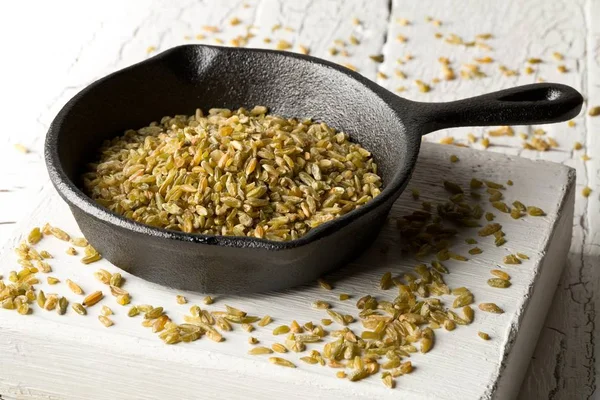 Uncooked, raw freekeh or firik, roasted wheat grain, in metal pan on white rustic table background — 스톡 사진