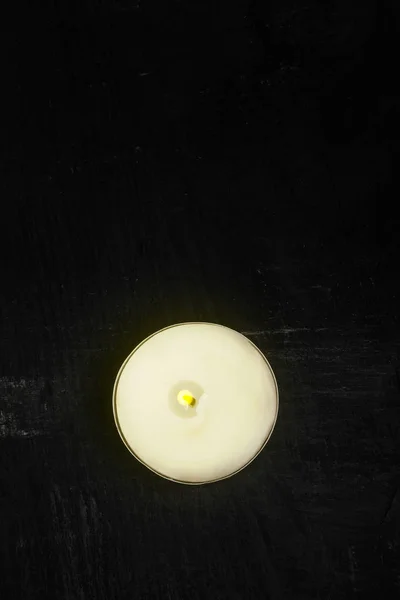 Single tealight candle burning on dark black background flat lay top view from above — Stock Photo, Image