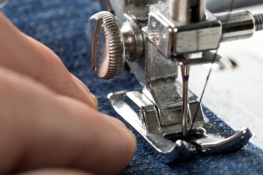 Dikiş makinesine kot pantolon diken adam. Kotları dikmek, moda tamiri, seçici odaklanma.