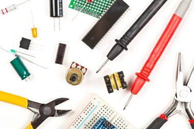 Beyaz zemin üzerinde farklı elektronik parçalar veya bileşenler, pense ve ölçüm aygıtı, rezistanslar, kapasitörler, diyot ve ik çipler, yukarıdan düz üst görünüm yatıyordu