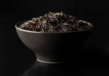 Siyah arka planda, siyah kasede pişmemiş, çiğ, siyah pirinç taneleri, seçici odak
