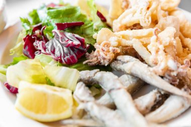 Karışık kızarmış balık oluşan bir close-up: Akdeniz balık, yumuşakçalar, limon ve karışık salata ile süslenmiş mürekkep