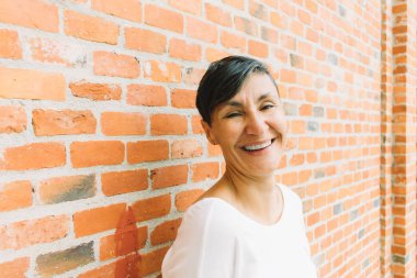 Kısa siyah saçlı, kameraya gülümseyen orta yaşlı bir kadın.