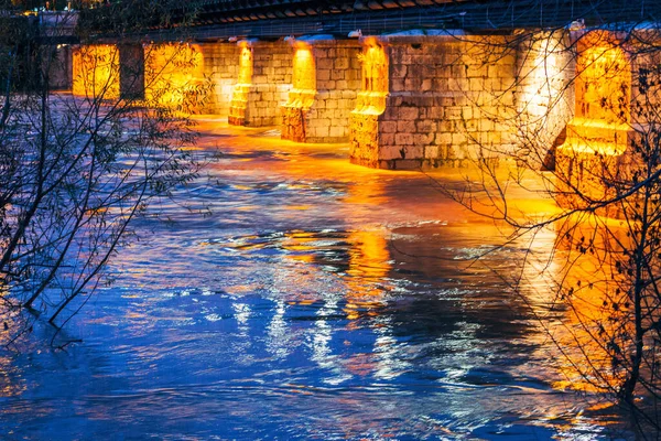Ponte de pedra iluminada sobre o rio à noite — Fotografia de Stock