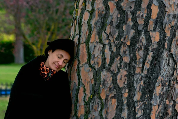 Woman with eyes closed with hat and black cape leaning on a tree — Stock Photo, Image