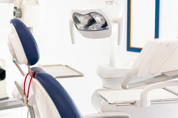 Diş kliniğinde beyaz duvarlı mavi bir dişçi koltuğu.