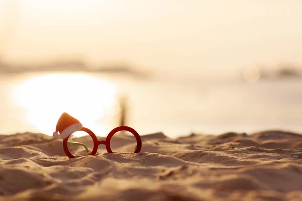 Óculos de Natal vermelho com chapéu de Papai Noel na praia ao pôr do sol bonito. Conceito de Natal . — Fotografia de Stock