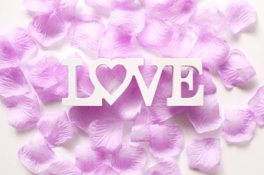 Çiçek yaprakları ve ahşap harflerden yapılmış aşk sözcüğüyle güzel beyaz bir zemin. Sevgililer Günü ve Kadınlar Günü için arka plan