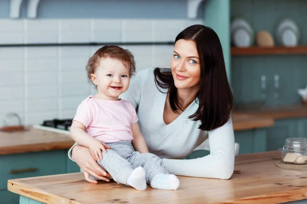 Glad liten bebis sitter på köksbordet med mamma och ler — Stockfoto
