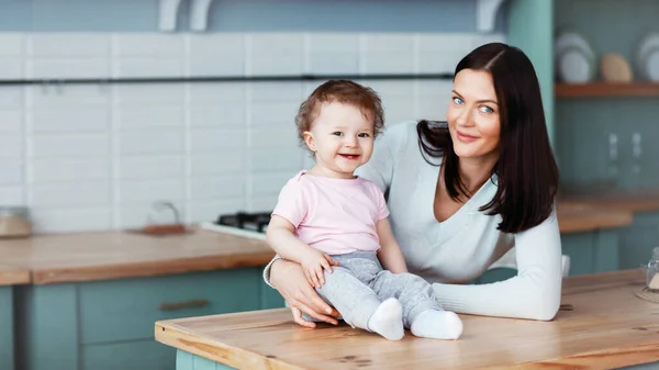 Glad liten bebis sitter på köksbordet med mamma och ler — Stockfoto