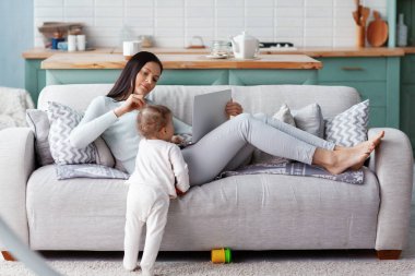Annesi, çocuğu oyun oynarken evde bir dizüstü bilgisayarda çalışıyor. İş ve aile kavramı.
