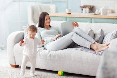 Annesi, çocuğu oyun oynarken evde bir dizüstü bilgisayarda çalışıyor. İş ve aile kavramı.