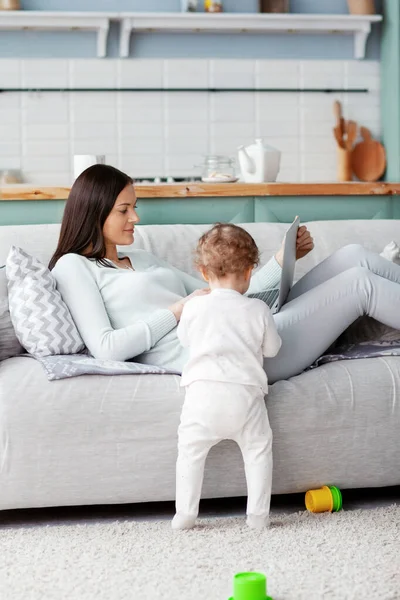 Mamma jobbar på en bärbar dator hemma medan hennes barn leker. Företags- och familjebegreppet. — Stockfoto